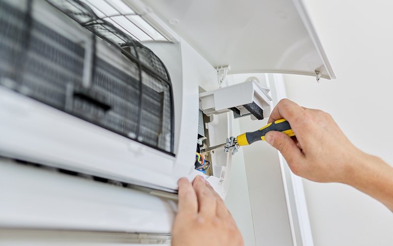 Technician using a screwdriver to service a home aircon unit.